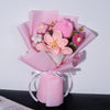 A bouquet of handmade crochet yarn flowers in pink and purple hues wrapped in sheer pink paper.