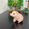 A small, pink pig figurine is displayed on a dark wooden surface with green foliage in the background.