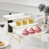 A gold-edged, three-tier rectangular serving platter stand displaying cupcakes and macarons on a white marble surface.