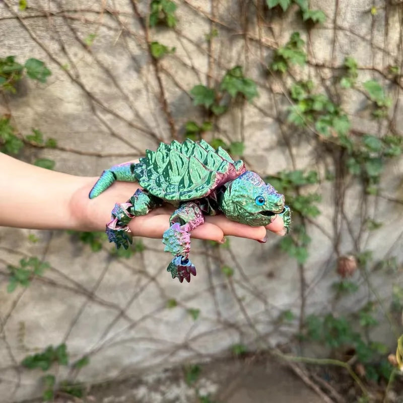 A hand holds a green and purple 3D printed alligator snapping turtle figurine with articulated joints against a textured wall