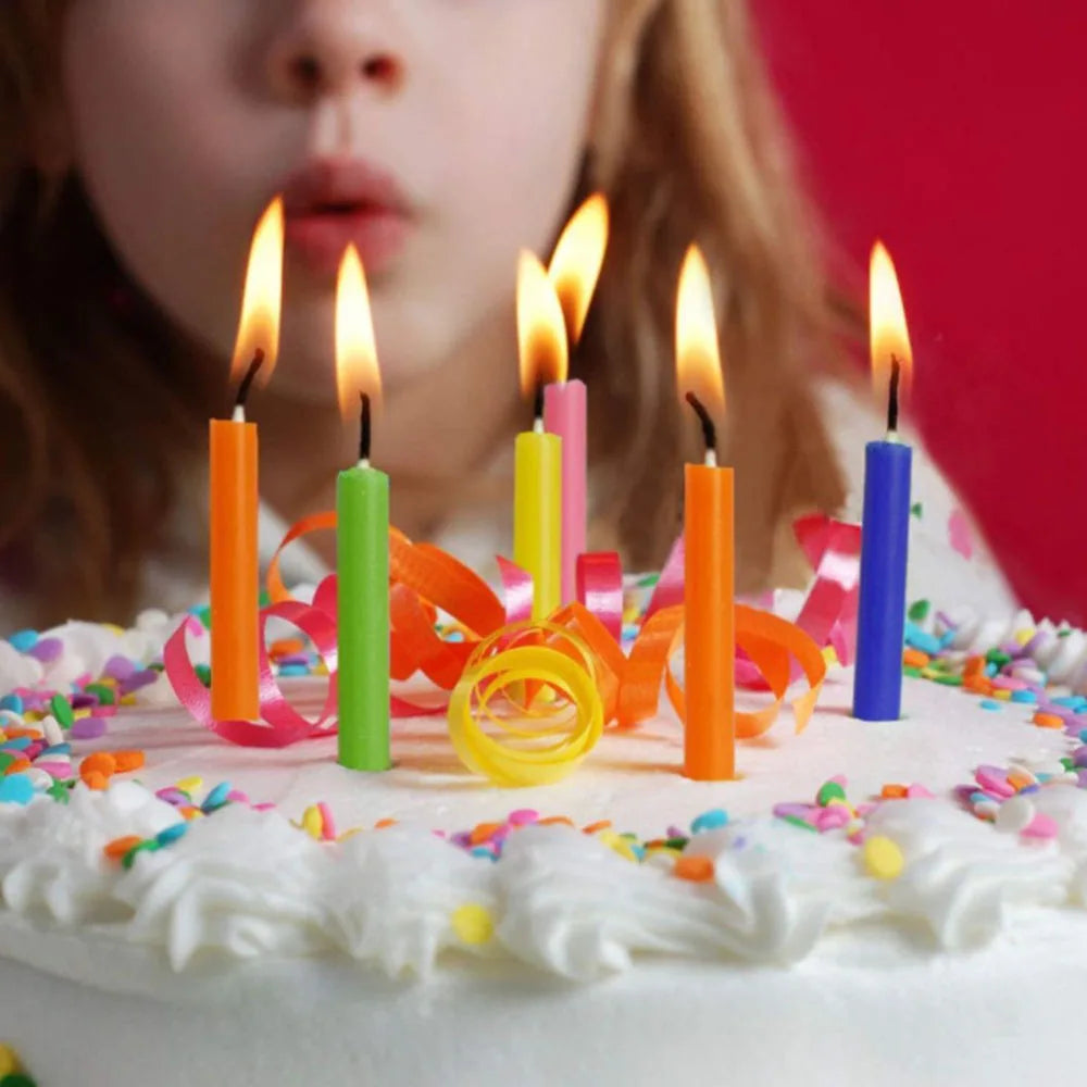 A cake decorated with white frosting and colorful sprinkles is surrounded by lit mini taper candles.