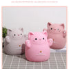 A pink cartoon cat piggy bank with a smiling face sitting on a light gray surface.