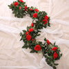 A lush garland of red silk roses and green leaves draped on sheer white fabric.