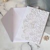 White laser cut wedding invitations featuring intricate scrollwork and gold pearl accents