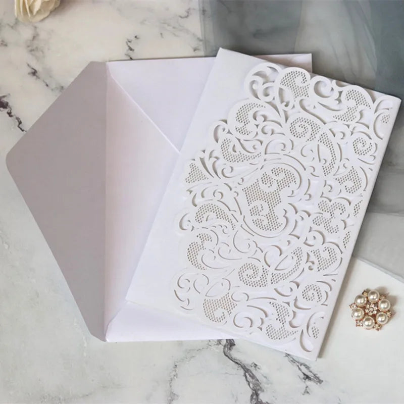 White laser cut wedding invitations featuring intricate scrollwork and gold pearl accents