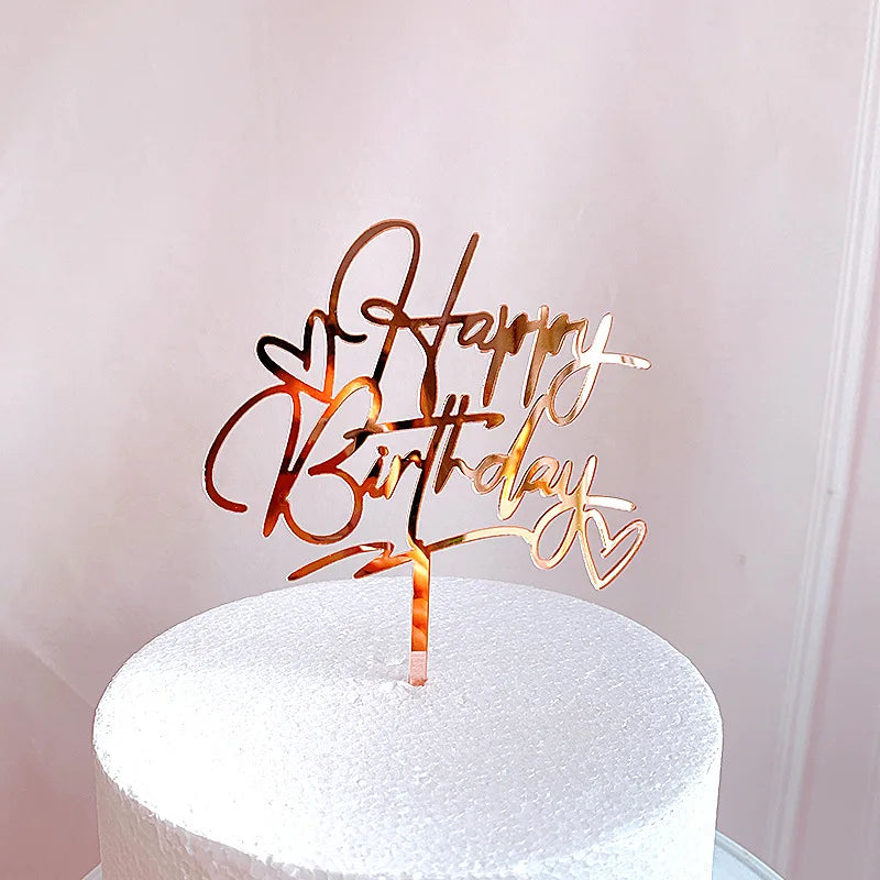 قالب كعكة عيد ميلاد من الأكريليك الذهبي يحمل عبارة 'عيد ميلاد سعيد' وتصميم قلب على كعكة بيضاء.