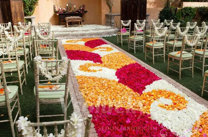 A long aisle decorated with silk rose petals in shades of pink, orange, and white for a wedding ceremony.