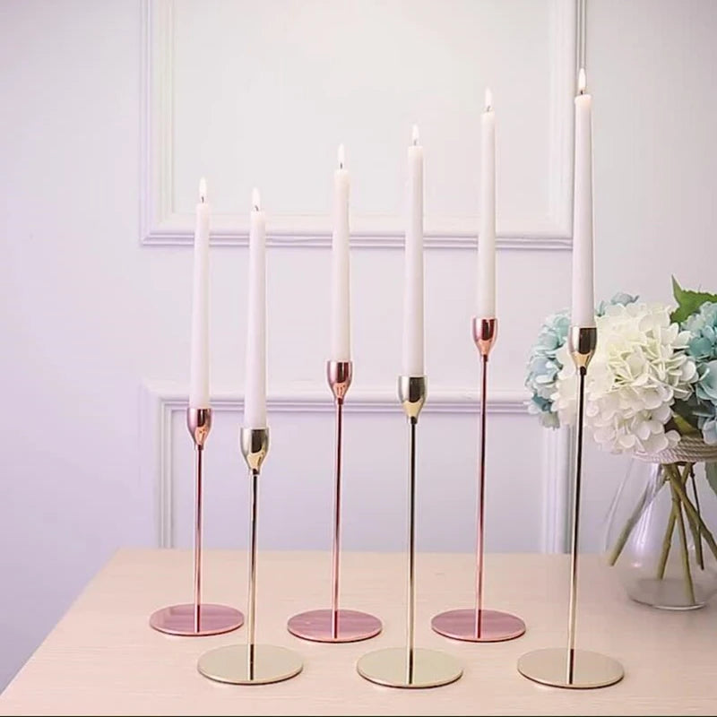 A set of tall, slender iron candles with pink accents displayed on a light wooden surface.