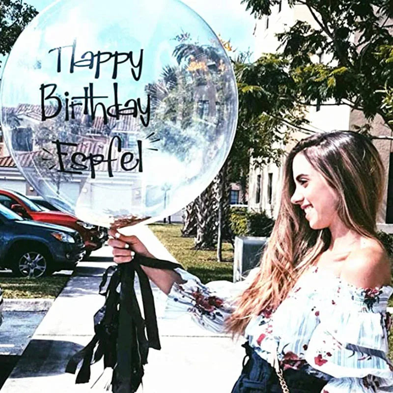 A young woman smiles while holding a large clear balloon with the text Happy Birthday Esfel to celebrate an event.