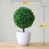 Artificial bonsai tree in a white pot with dense green foliage, shown against a light background.