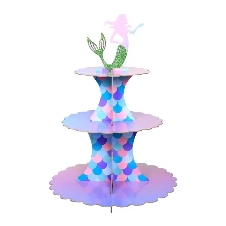 A three-tier cardboard cupcake stand decorated with purple and green glitter, featuring a pink fairy figure.