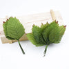 A set of twelve silk leaf artificial plant stems used for vases, displayed on a wooden board.