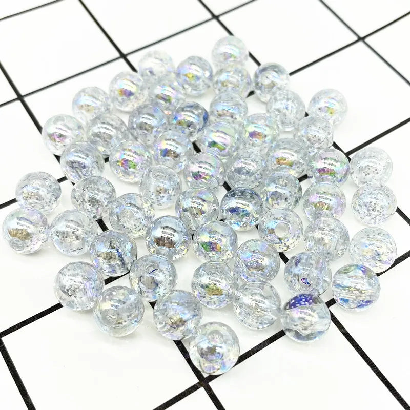A pile of clear iridescent acrylic round beads for jewelry making scattered on a grid background.