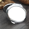 A silver mini double-sided folding makeup mirror is shown on a dark wooden surface.