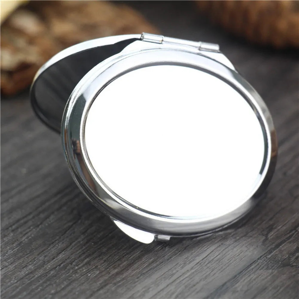 A silver mini double-sided folding makeup mirror is shown on a dark wooden surface.