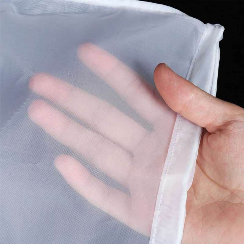 A hand is holding a clear, fine mesh nylon filter bag, demonstrating its texture and use.