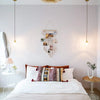 A white bedroom featuring a bed with macrame photo displays and neutral bedding.
