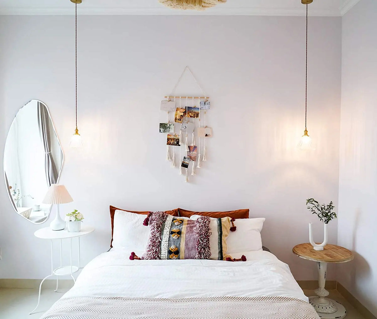 A white bedroom featuring a bed with macrame photo displays and neutral bedding.