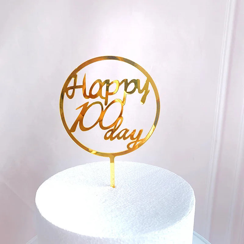 قالب كعكة عيد ميلاد من الأكريليك الذهبي يحمل عبارة 'عيدك المئة يوم' على كعكة بيضاء.