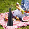 A black automatic electric fly repellent fan is displayed on a red and white checkered cloth with fruit and a woven basket in