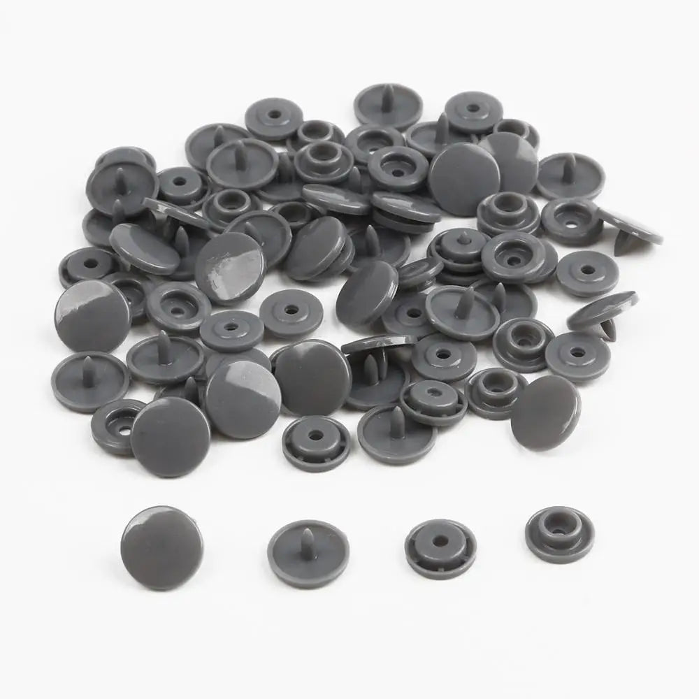 A pile of assorted dark gray snap buttons, measuring 12mm and 10.5mm, for crafting.