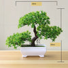 Artificial bonsai tree in a white rectangular pot with green foliage, displayed on a wooden surface.