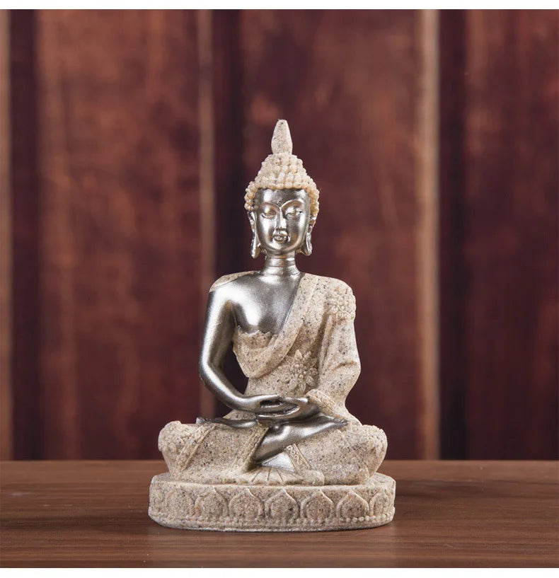 A handcrafted resin Buddha statue in silver color sitting in meditation pose on a wooden surface.