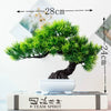 Artificial bonsai tree in a white pot with dark roots, displayed on a book.