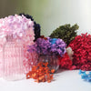 A collection of dried hydrangea flowers in shades of pink, purple, red, and green arranged on a white surface.