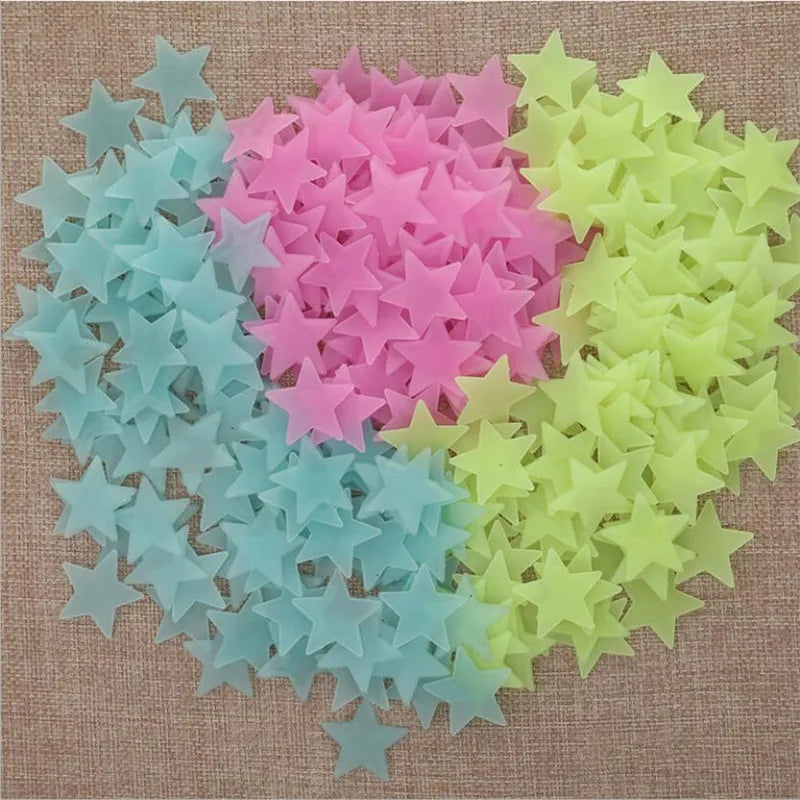A collection of 50 glow-in-the-dark star wall stickers in various shades of pink, blue, and green scattered on a beige surfac