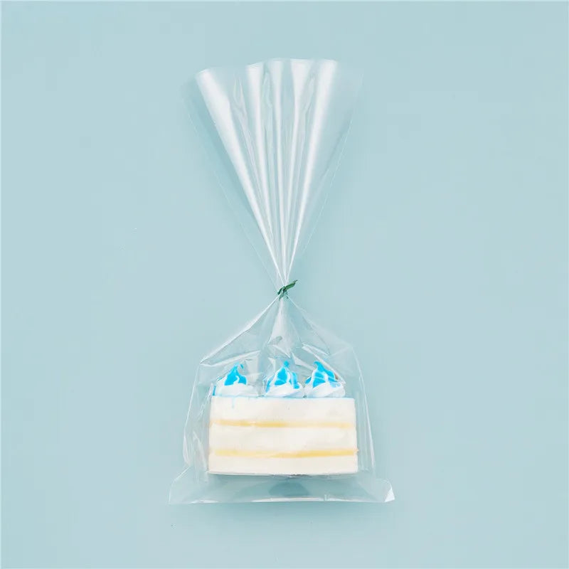A clear cellophane gift bag with a gold twist tie holds a rectangular white candle.