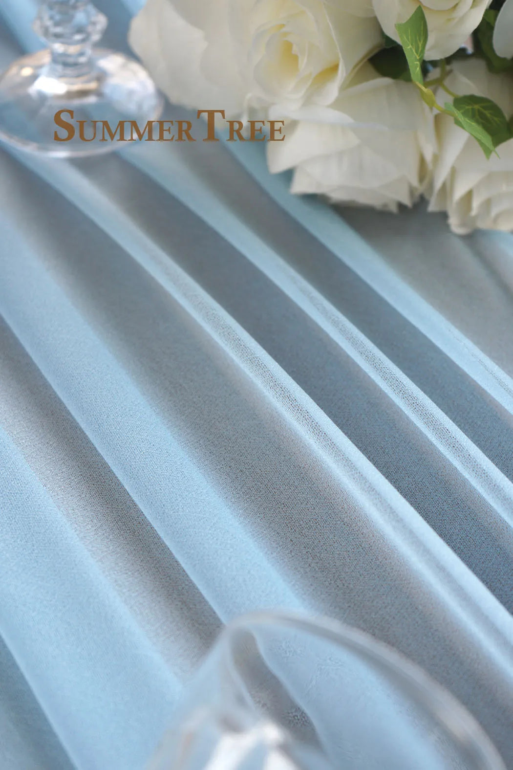 Light blue chiffon fabric draped elegantly with white roses and greenery.