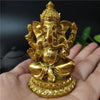 A golden handcrafted resin statue of Ganesha is held in a person's hand.