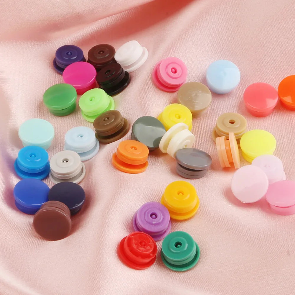 A collection of assorted snap buttons in various colors including pink, purple, green, yellow, and brown, laid out on a pink 