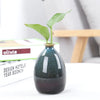 Handbemarter Keramikblumenvase mit grünem Pflanzen, auf weißer Oberfläche.