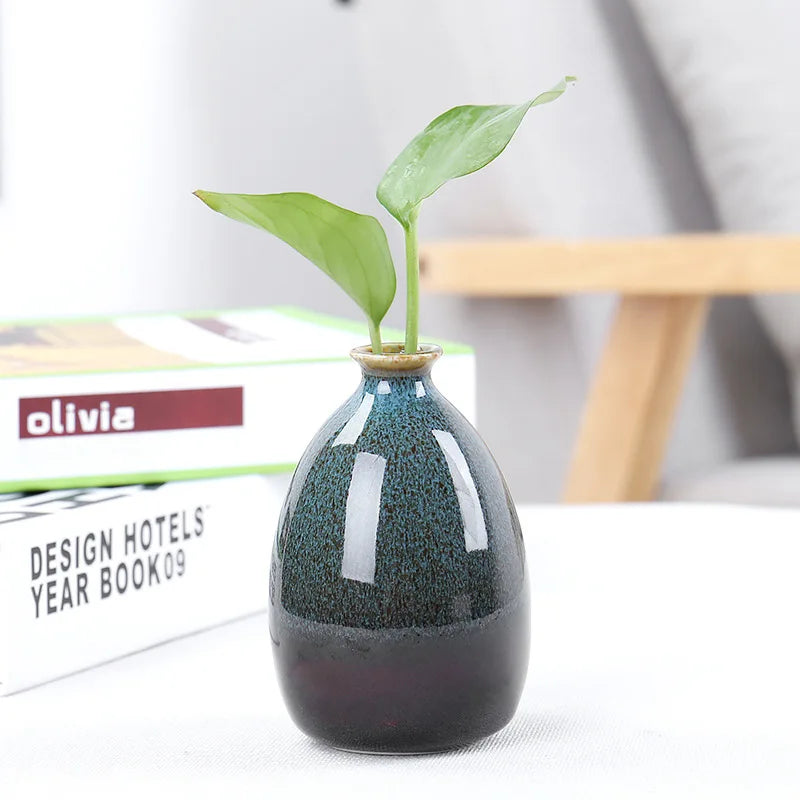 Handbemarter Keramikblumenvase mit grünem Pflanzen, auf weißer Oberfläche.