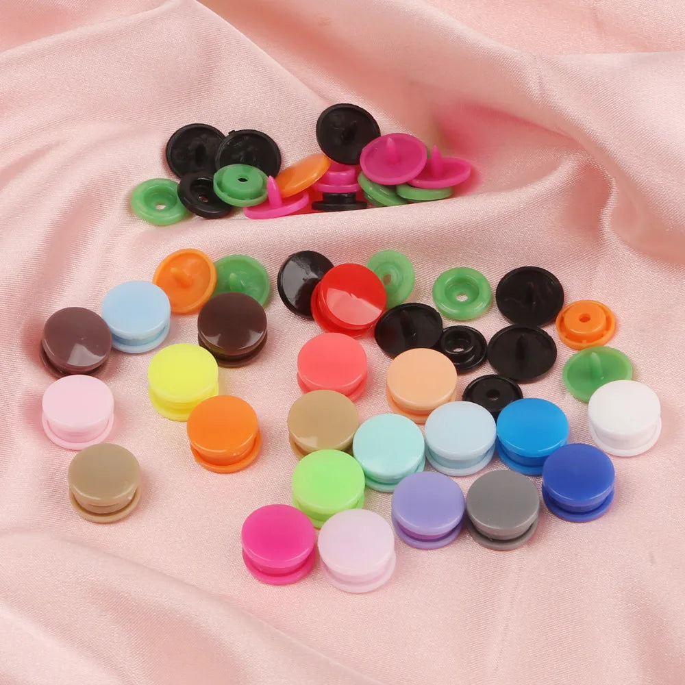 Assorted snap buttons in various colors including black, green, pink, and orange arranged on a pink fabric.