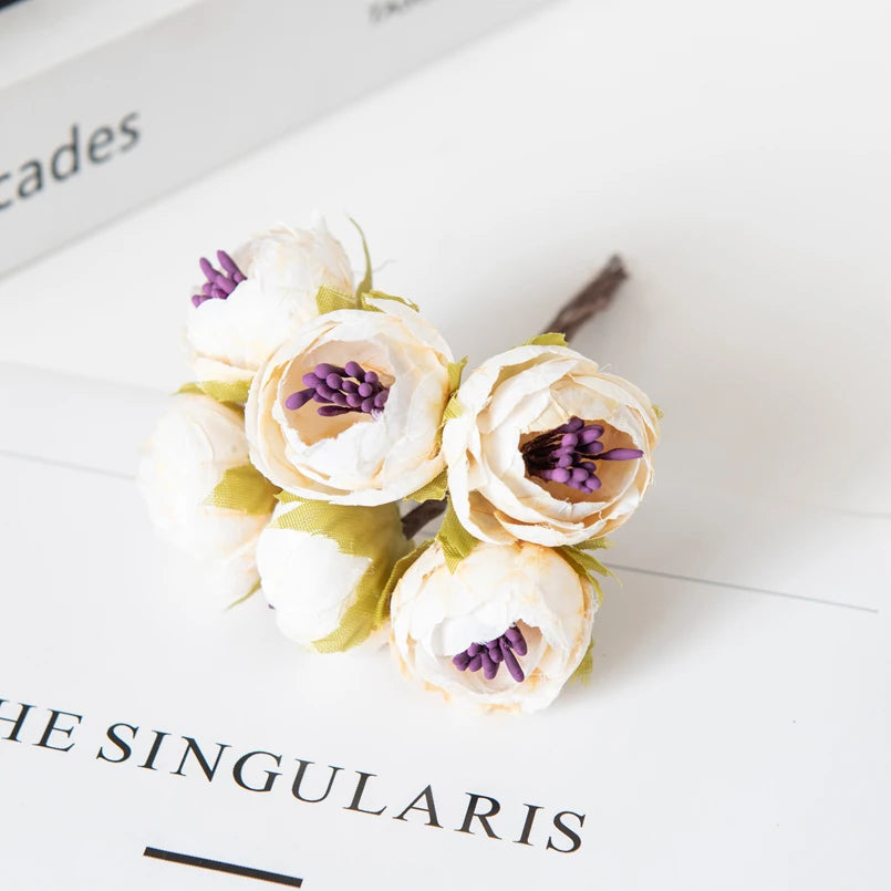 Eine Ansammlung von weißen und blassrosa Kunstseide-Rosen mit violetten Zentren auf einer weißen Oberfläche.