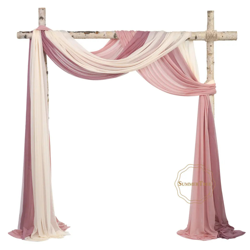A sheer chiffon fabric drape in shades of pink and ivory is displayed hanging from a wooden cross structure.