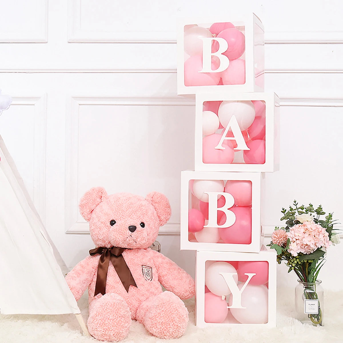 Pink teddy bear sitting next to letter balloon boxes for baby shower decorations