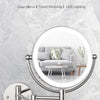A round, wall-mounted LED makeup mirror with a silver frame and adjustable arm is shown against a marbled background.