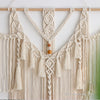 Cream macrame wall hanging tapestry with fringe and tassels suspended from a wooden rod.