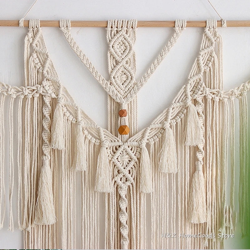 Cream macrame wall hanging tapestry with fringe and tassels suspended from a wooden rod.