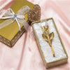 A gold-colored box with a ribbon and a crystal rose artificial flower in a velvet insert.