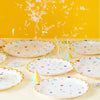 A collection of colorful, cartoon-themed disposable paper plates scattered on a light surface against a yellow background.