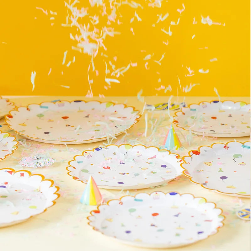 A collection of colorful, cartoon-themed disposable paper plates scattered on a light surface against a yellow background.