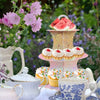 A 3-tier cardboard cupcake stand decorated with watermelon slices and cupcakes set on a white table.