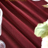 A close-up of deep burgundy sheer chiffon fabric draped on a table with a glass and a white flower.