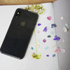 A black smartphone lies on a white page surrounded by scattered dried purple and green hydrangea petals.