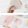 A hand holds a stack of pink and green decorative memo pads and cards for a journal or stationery set.